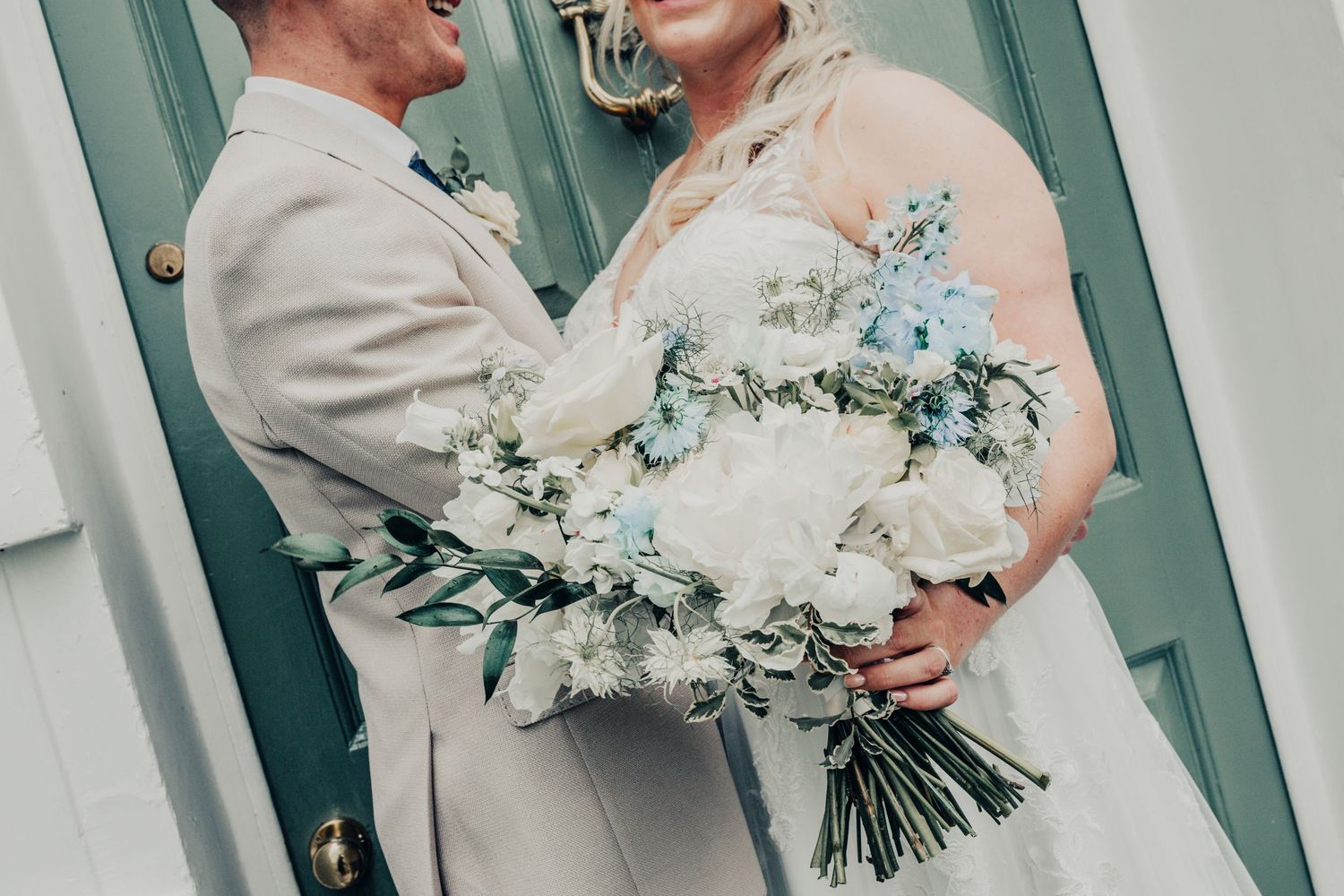 Close up of couple with white and blue flower bouquet against turquoise door.