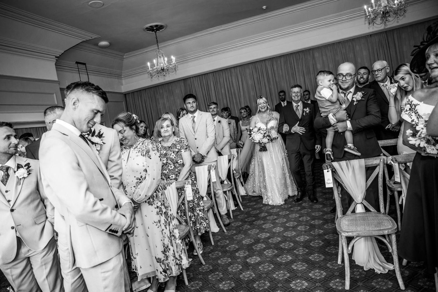 Wedding ceremony guests gathered in a formal ballroom with chandeliers and elegant decor.