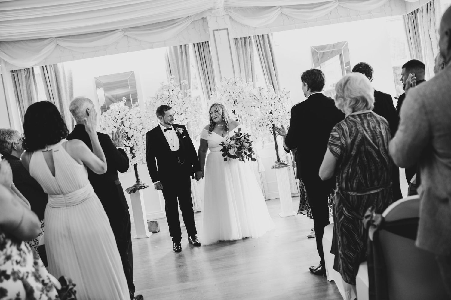Wedding guests mingle and socialize during a reception in a bright white tent venue.