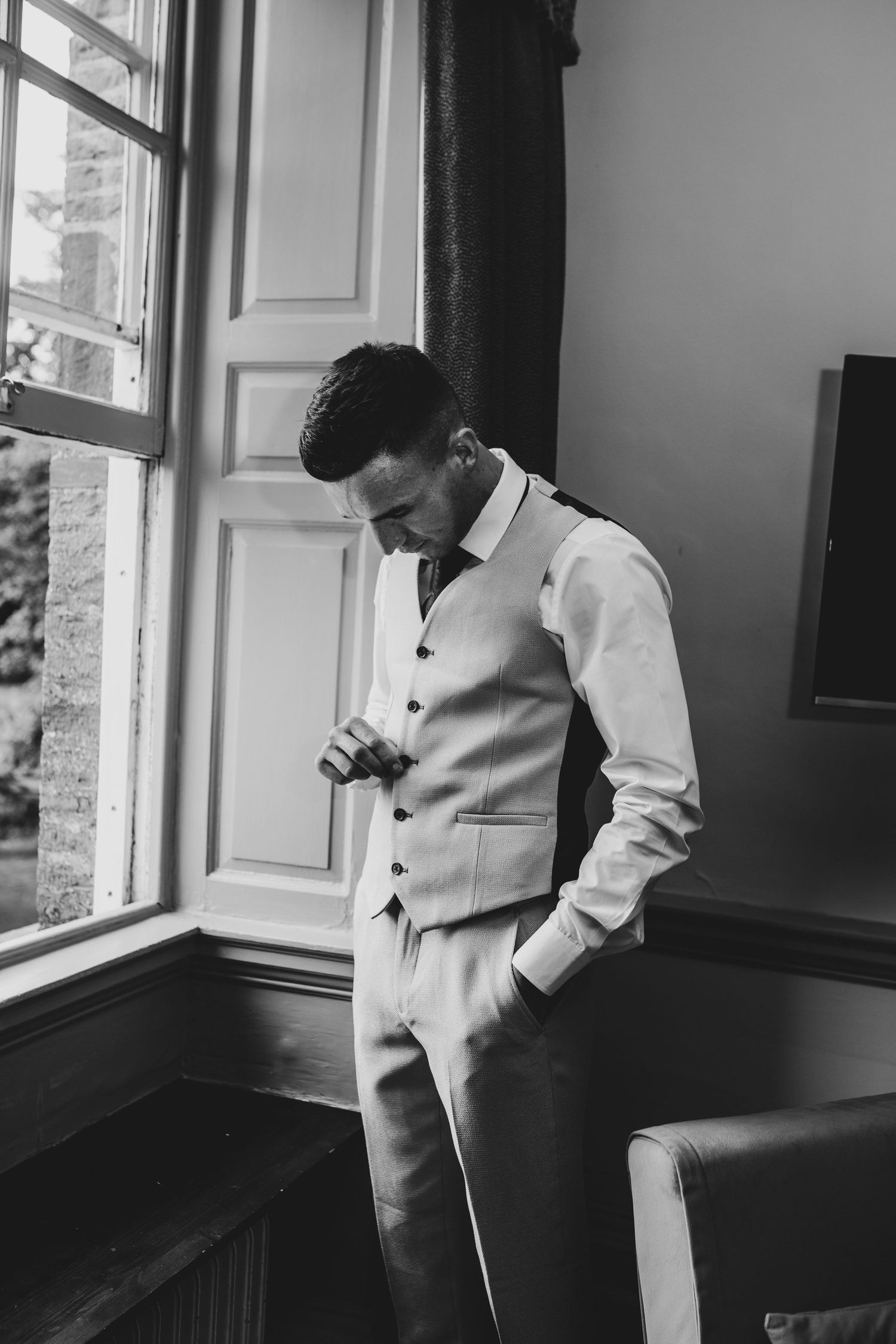 Groom looking down while getting ready by window.
