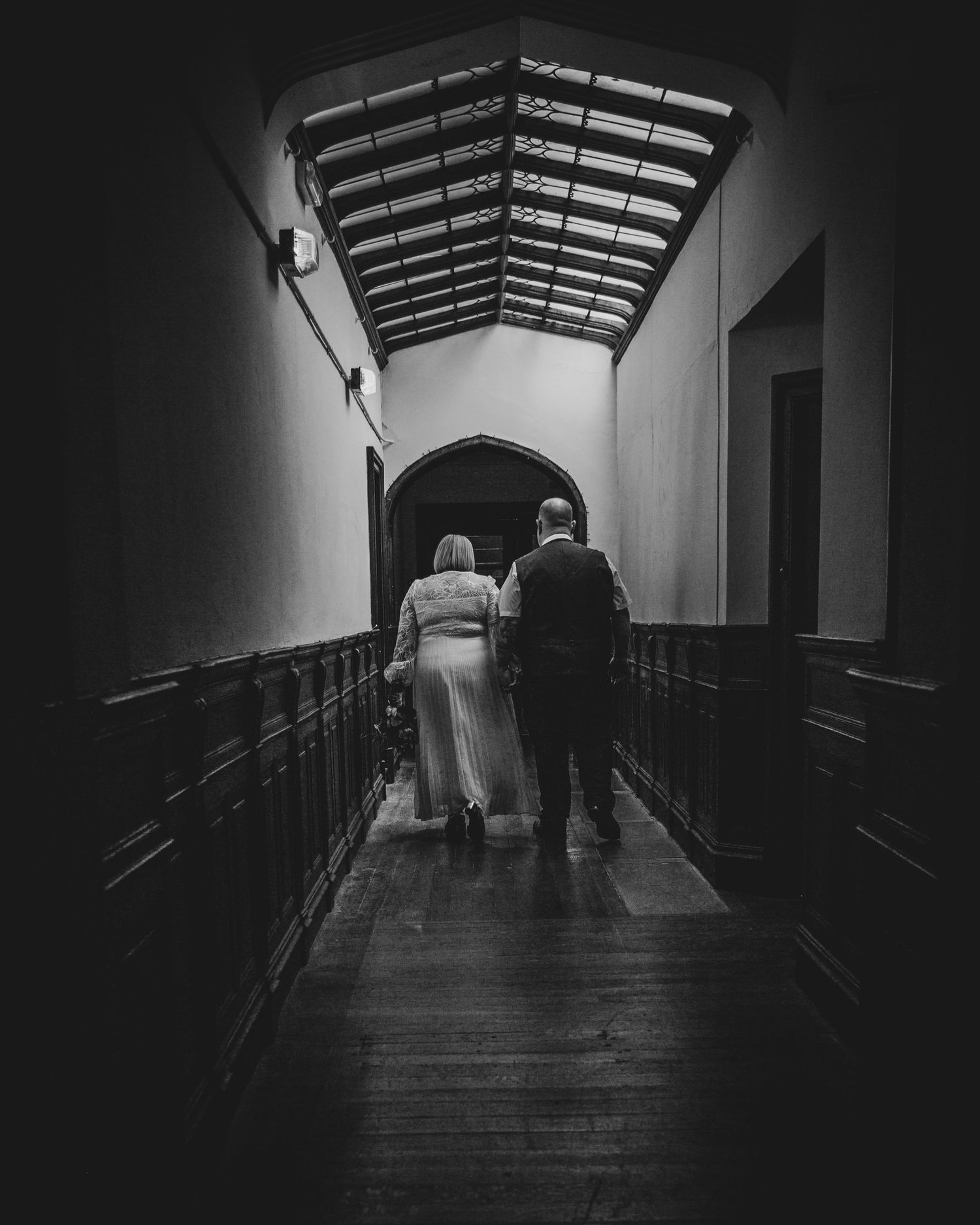 A silhouetted couple walks down a dramatically lit corridor with an arched glass ceiling.