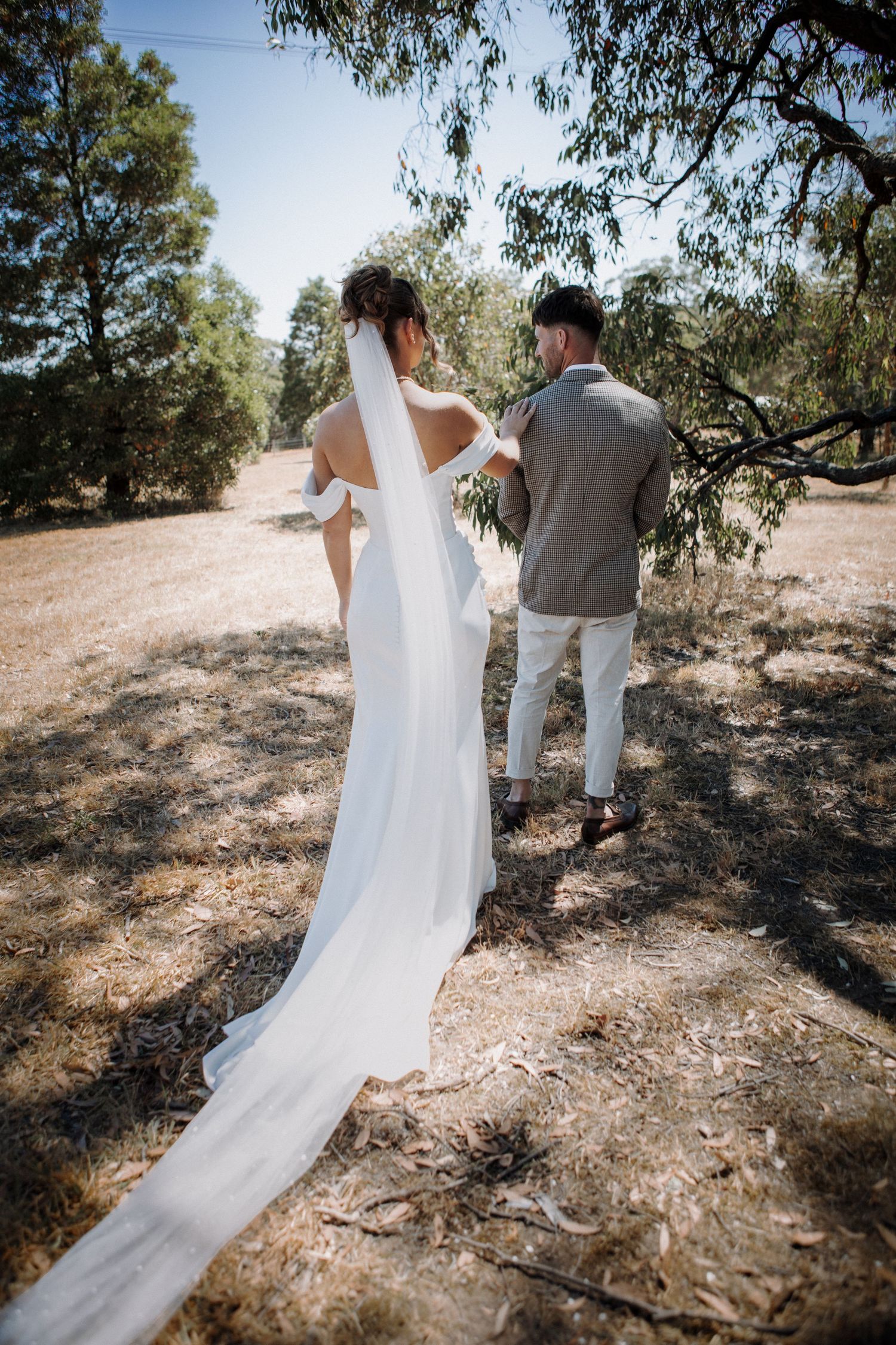 Bride and groom walking hand in hand through a sunlit Australian bush landscape.