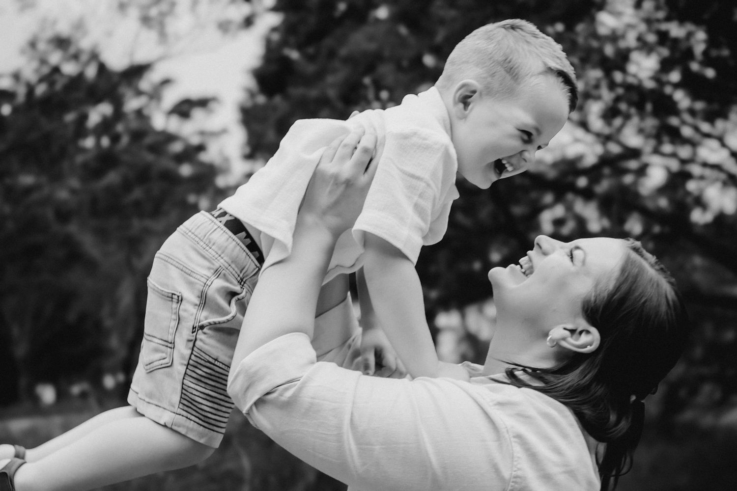 A black and white photo of a laughing mother lifting her joyful baby into the air.