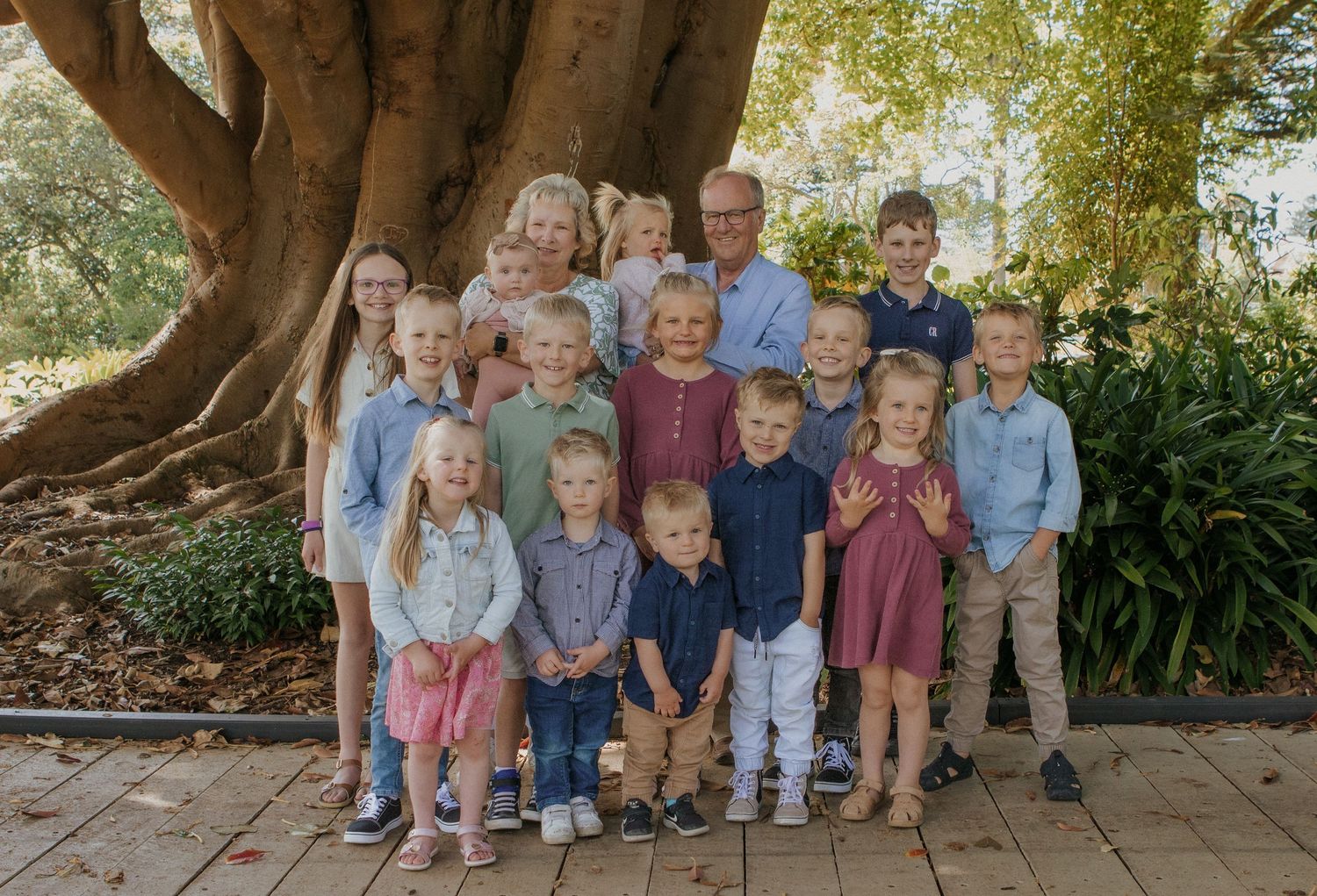 Grandparents surrounded by their grandchildren in a cheerful group photo beneath a large tree at Warrnambool Botanical Gardens.