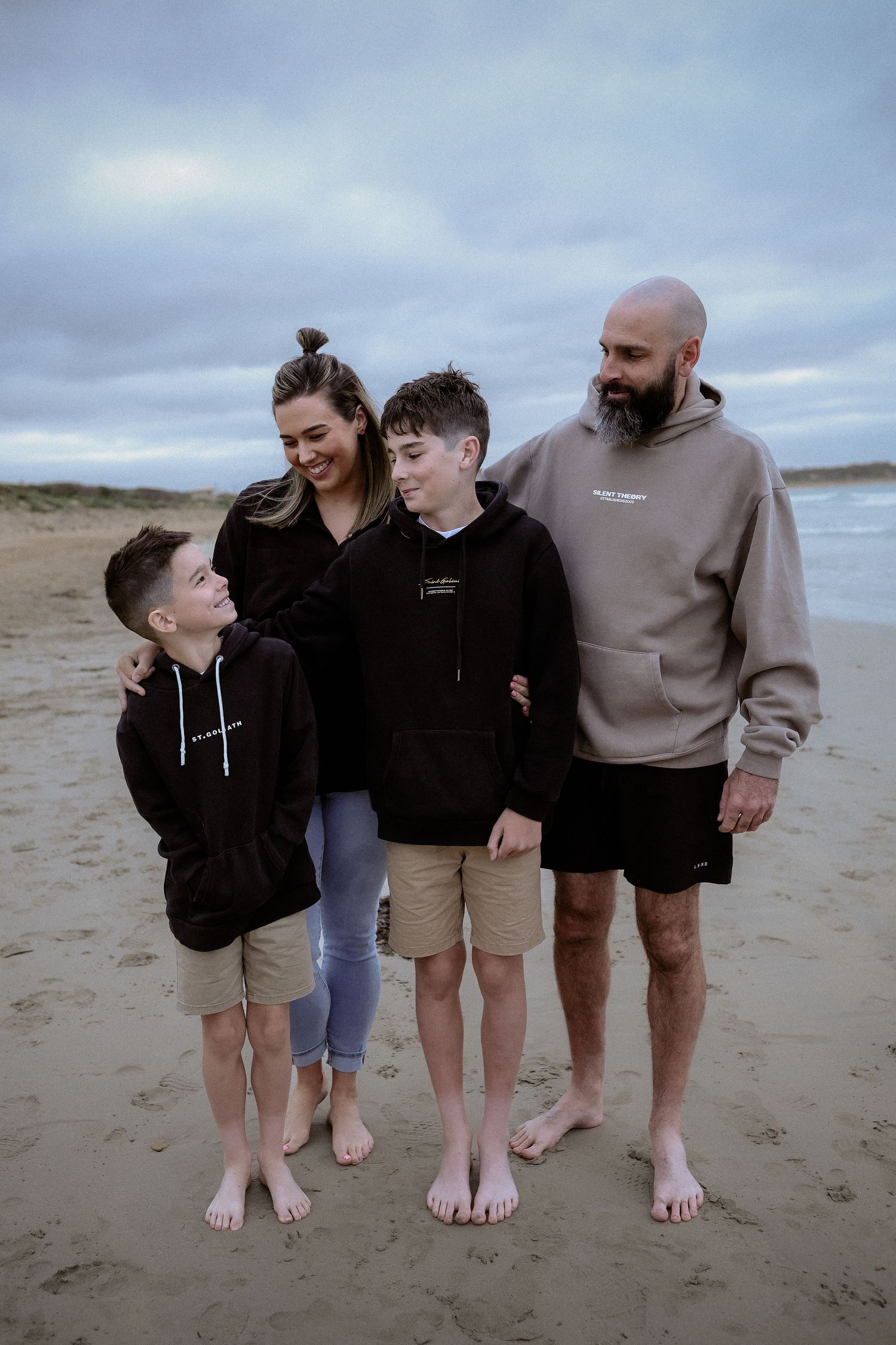 Family of four posing at Warrnambool beach, two boys with parents in casual hoodies on overcast day.