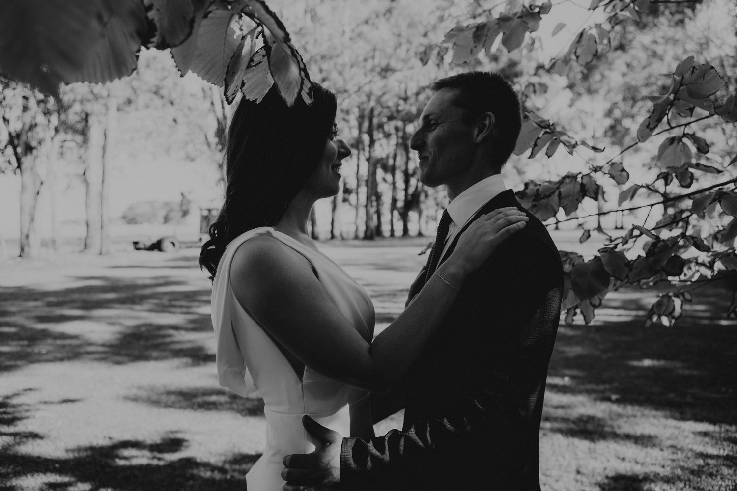 Black and white photo of a couple sharing a romantic moment under leafy branches at an outdoor wedding ceremony.