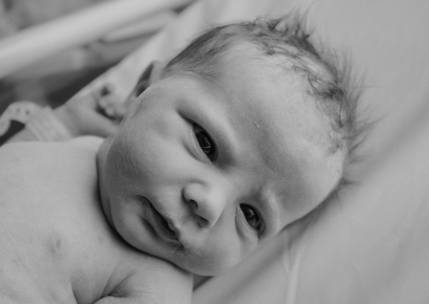 Close-up black and white portrait of smiling newborn baby lying on white blanket.