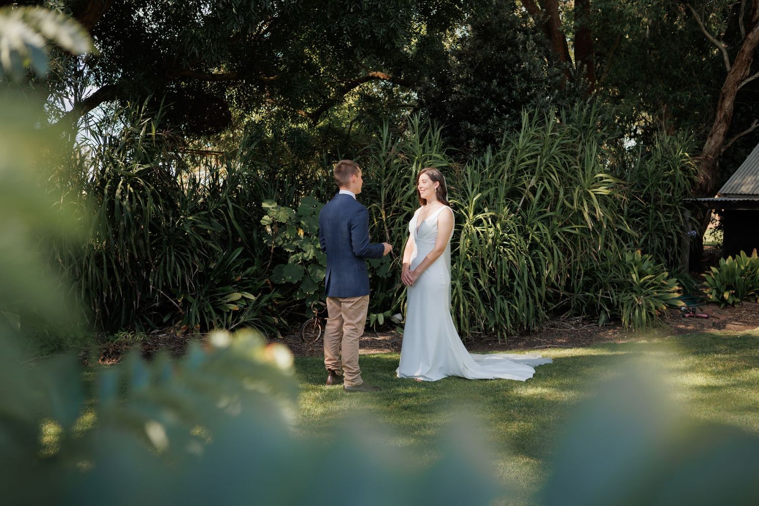 Bride and groom exchange vows outdoors surrounded by lush green tropical garden foliage during intimate wedding ceremony.