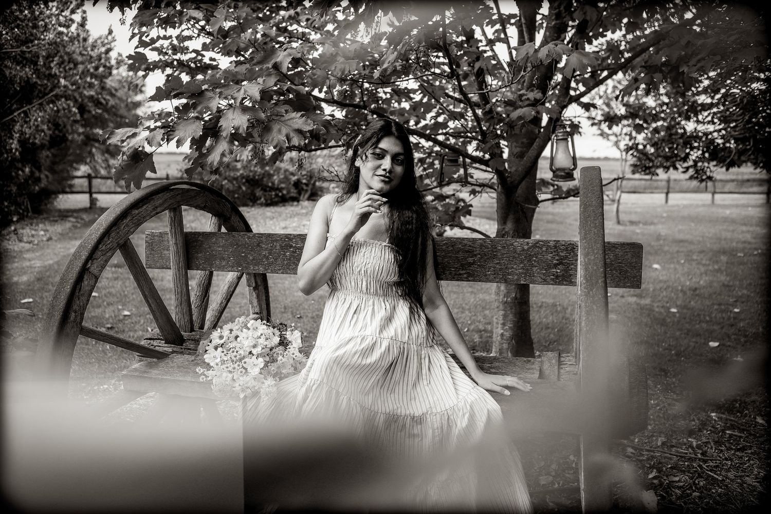 Black and white portrait of woman in white dress sitting by vintage wagon wheel outdoors at Warrnambool Botanical Gardens.