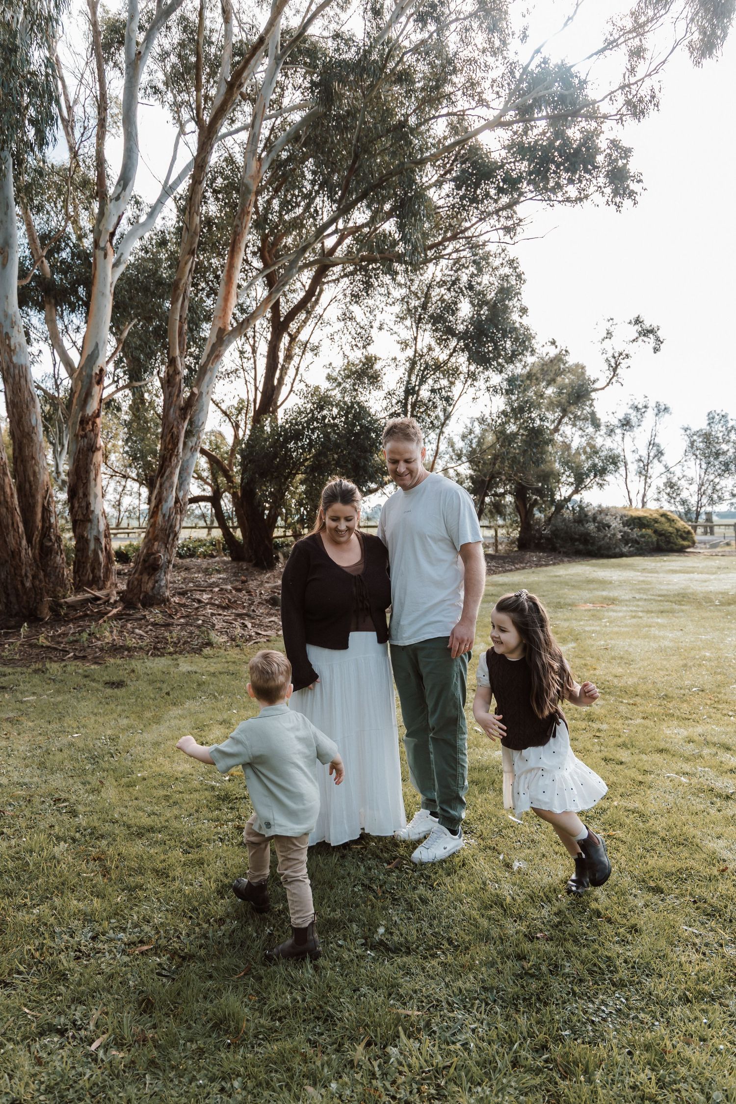 Family of four enjoying outdoor time together on green grass with tall eucalyptus trees in background.