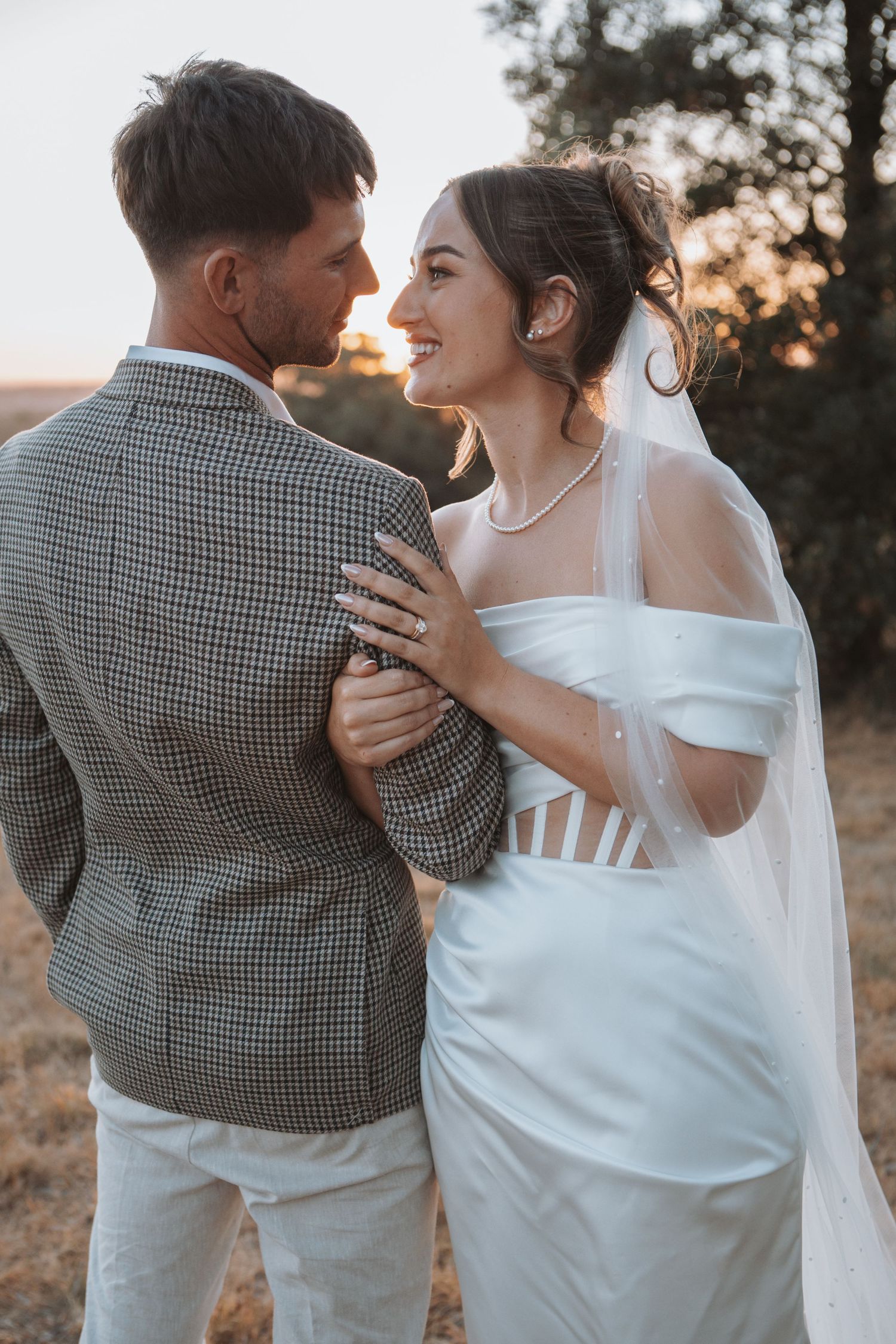 Bride and groom share a romantic moment at sunset, smiling at each other in wedding attire.