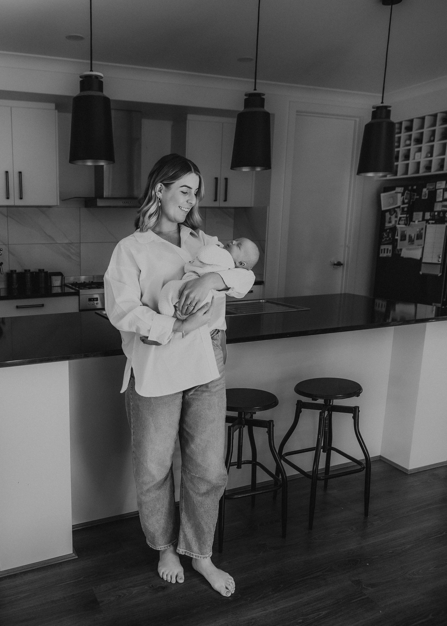 Black and white photo of a mother cradling her newborn baby in a modern kitchen.