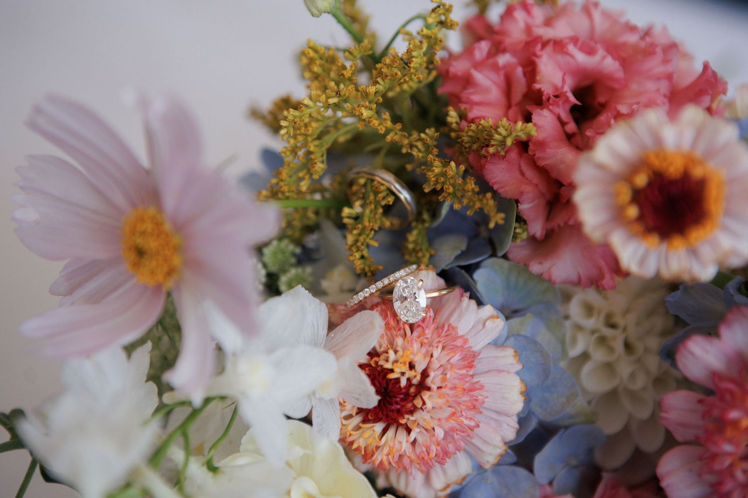 Diamond engagement ring resting on colorful wedding bouquet with pink, orange, and blue flowers.