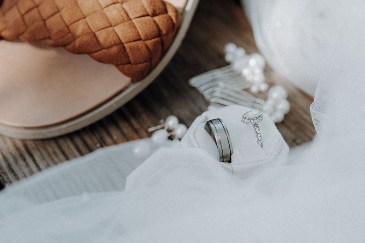 Wedding rings and a diamond engagement ring displayed on white fabric beside pearl accessories and elegant bridal shoes.
