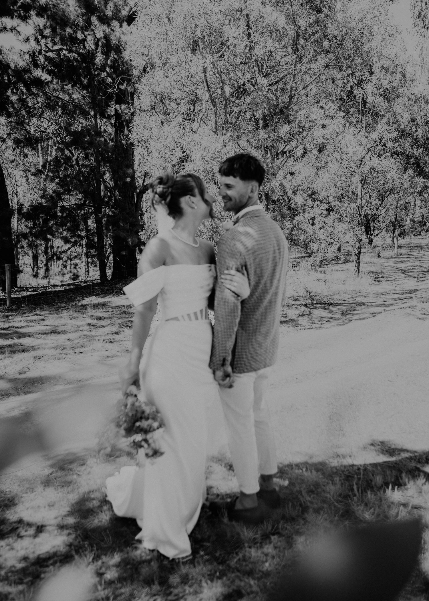 Black and white photo of bride and groom embracing among trees on their wedding day.