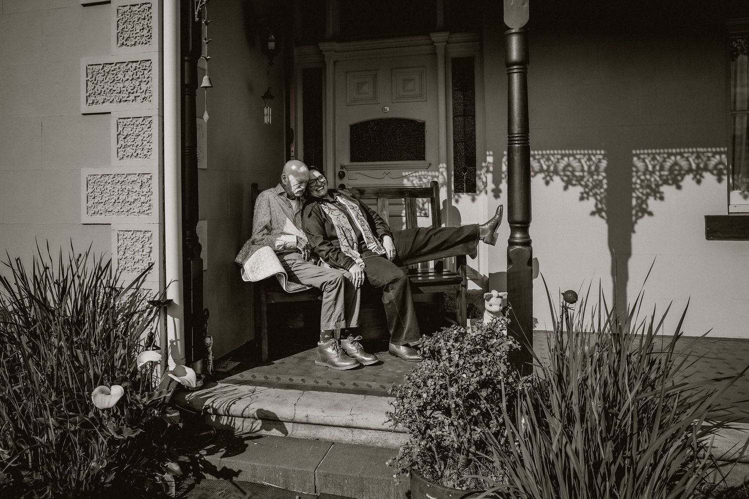 Black and white photo of elderly couple sitting together on a home porch steps.