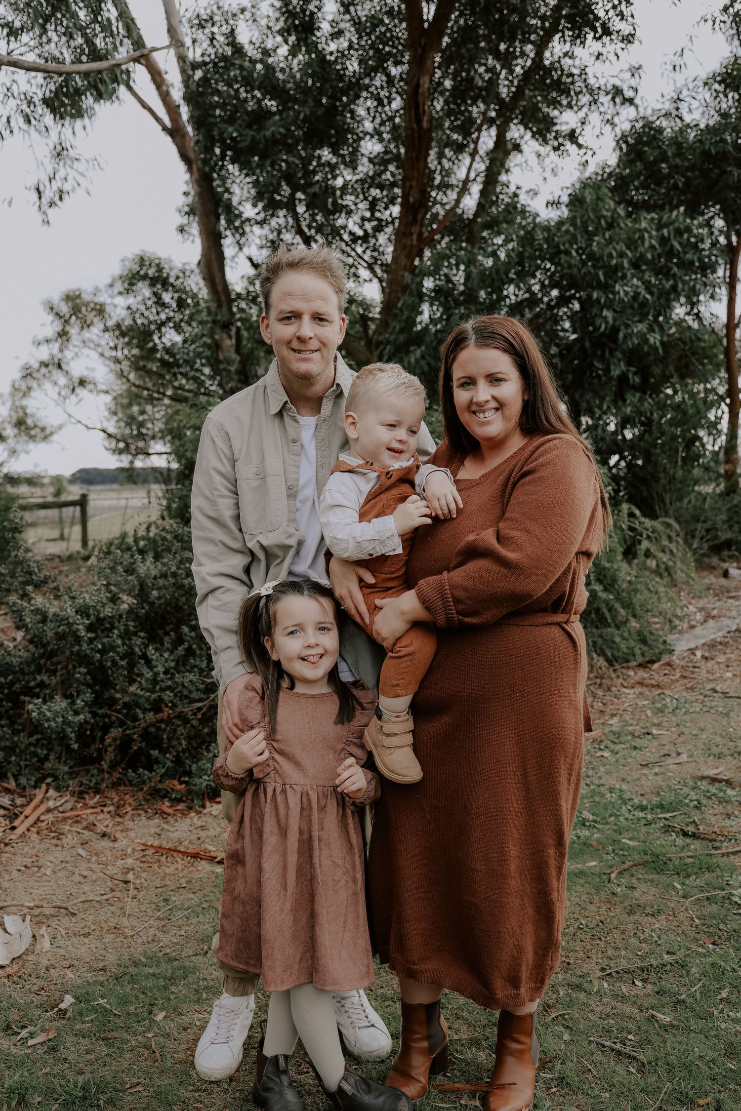 Happy family of four poses outdoors among eucalyptus trees in autumn tones.