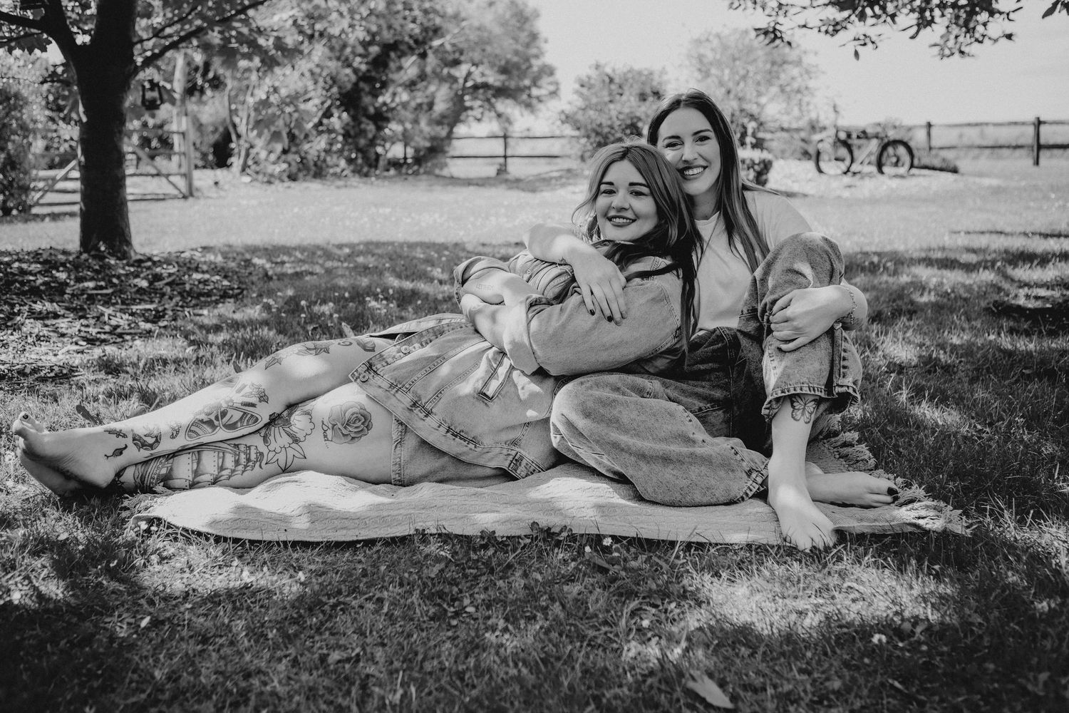 Black and white photo of two women laughing and relaxing together on blanket in park.