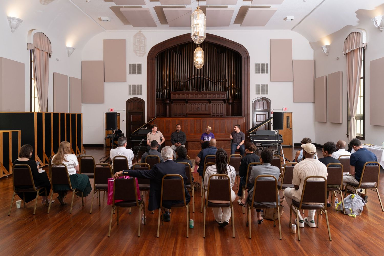 Wide view of a church or concert hall interior with chairs arranged in rows and arched doorways.
