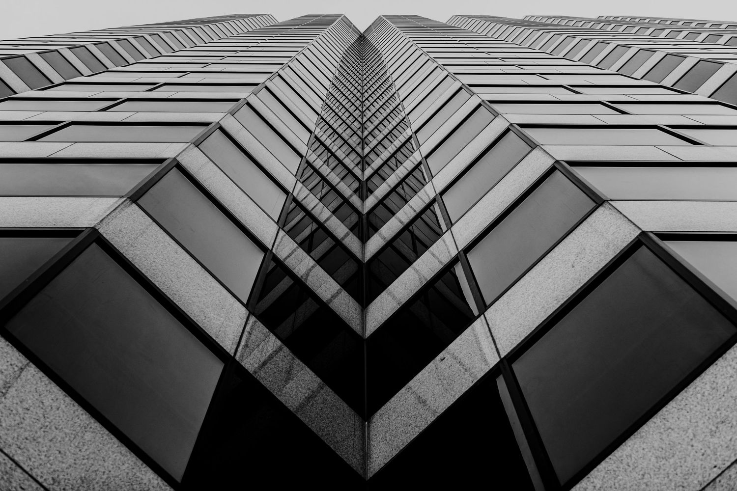 Dramatic upward view of modern building facade with repeating geometric windows in black and white.