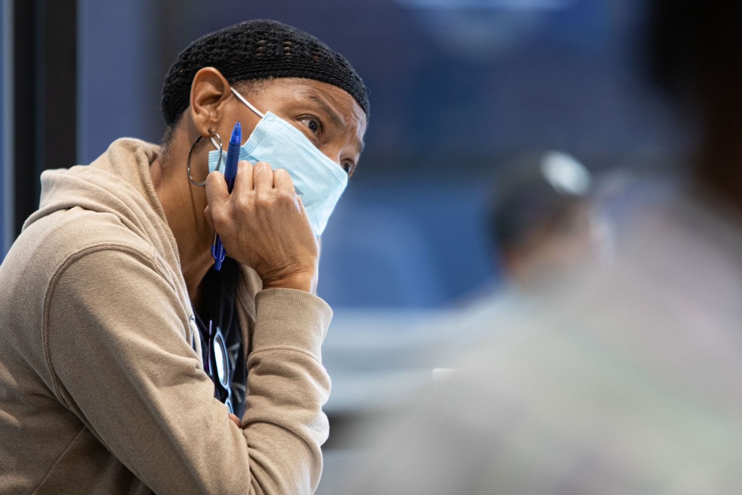 Someone wearing a face mask and hoodie sits while adjusting their mask during a pandemic.