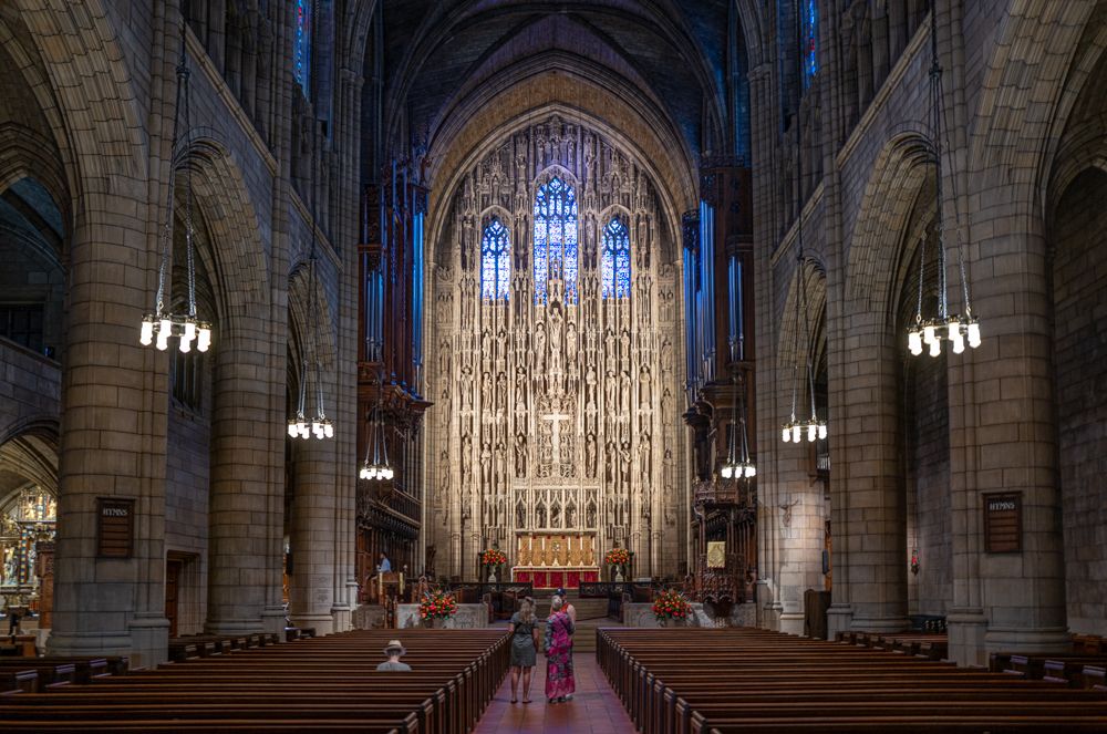 Gothic cathedral interior with stunning stained glass windows, vaulted ceilings, and rows of wooden pews.