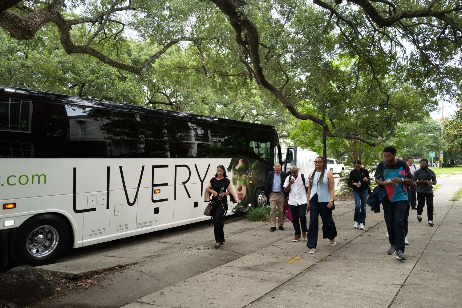 People walking under large oak trees with Spanish moss along a path near a white vehicle.