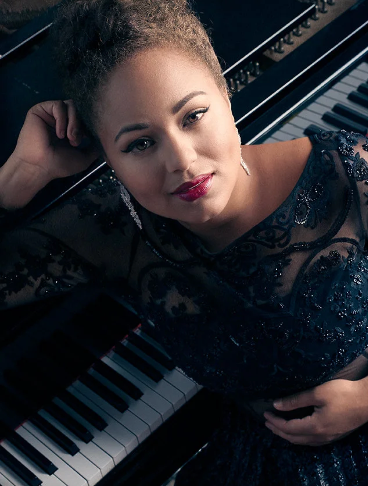 Elegant portrait of a performer in a beaded dress resting against a grand piano.