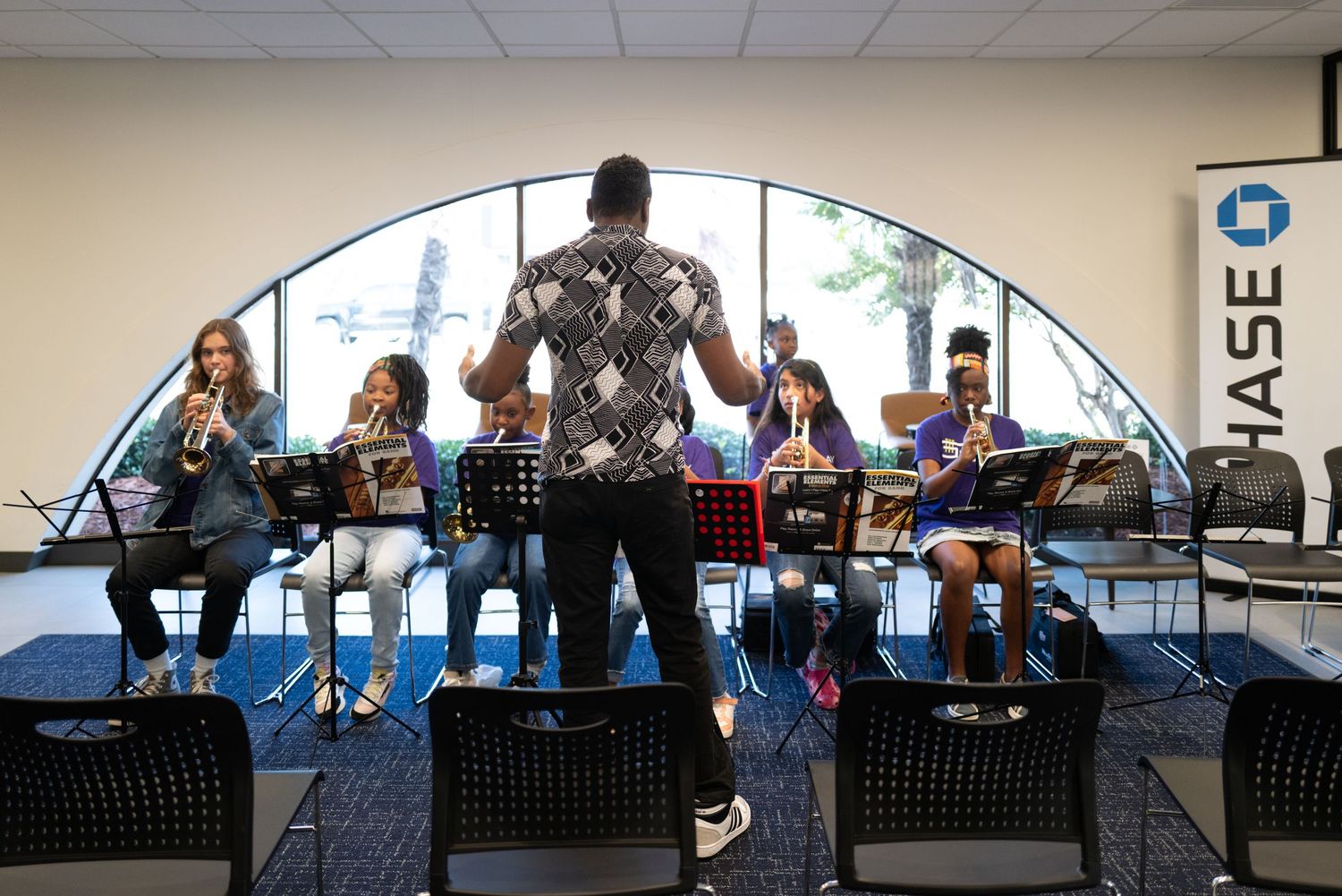 A band performs on stage at a Chase corporate event with arched windows behind them.