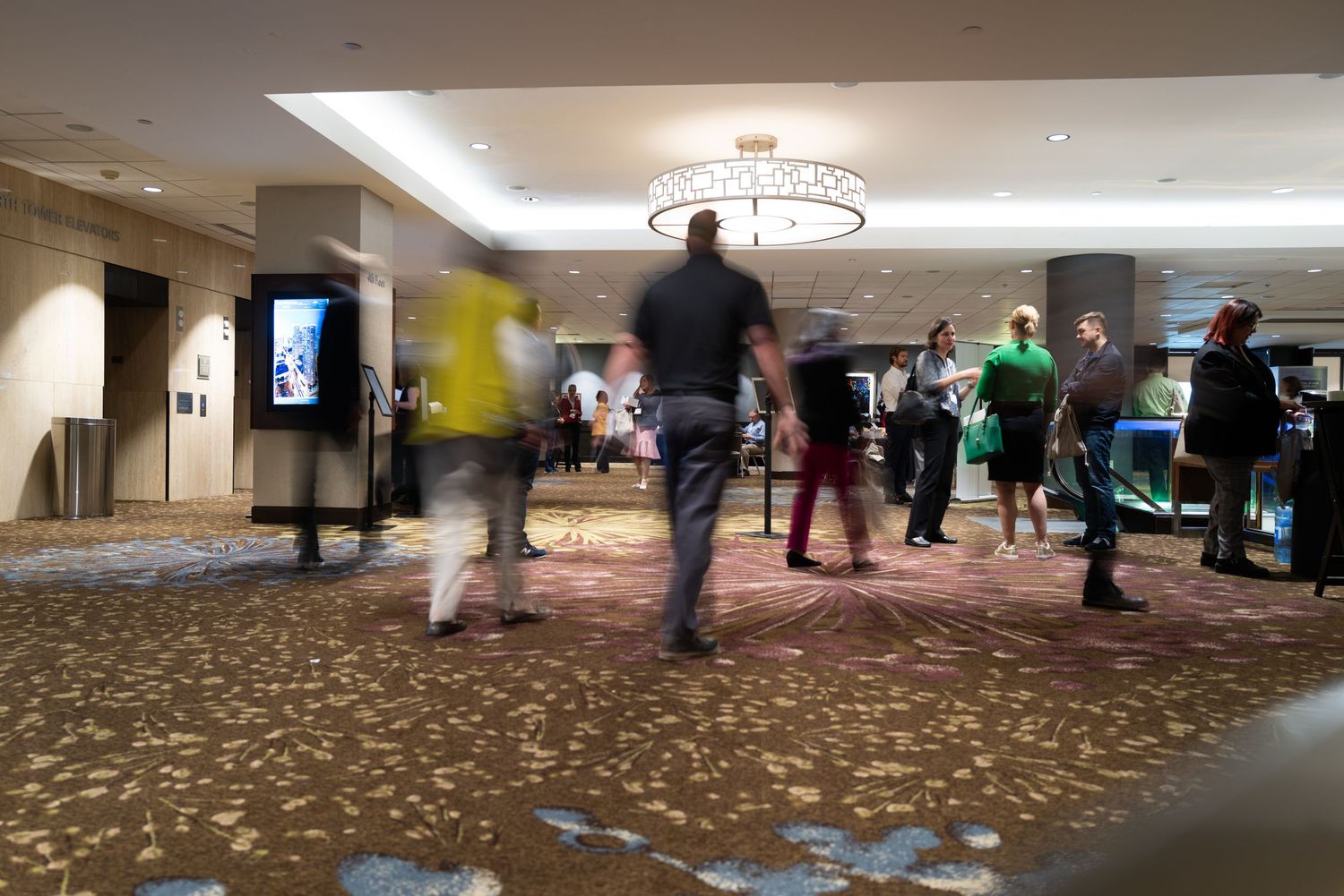 People in motion at a busy conference venue with patterned carpet.