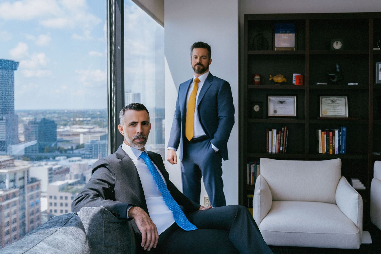 Professional in a blue suit stands in a modern office interior with white furniture and city views.