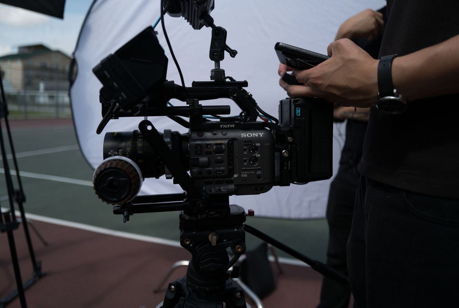 A professional cinematographer operating a cinema camera on a tripod at an outdoor film production set.
