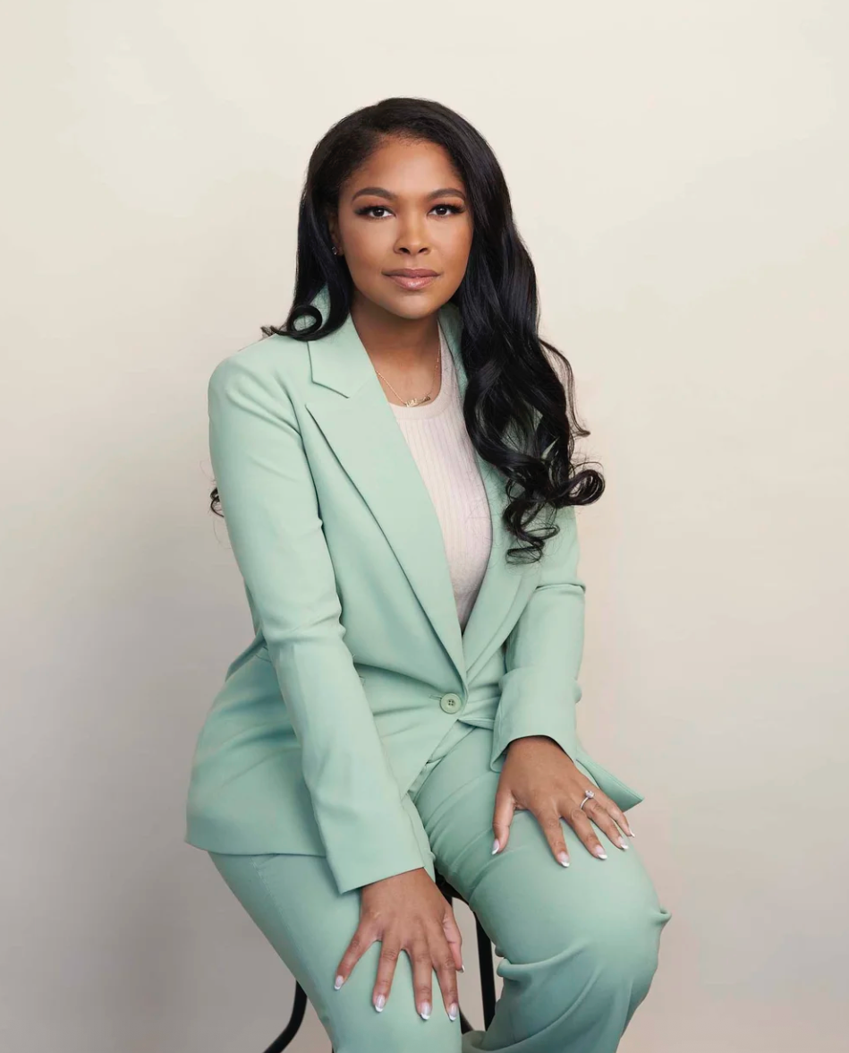 Professional portrait of someone wearing a stylish mint green business suit seated against a neutral background.