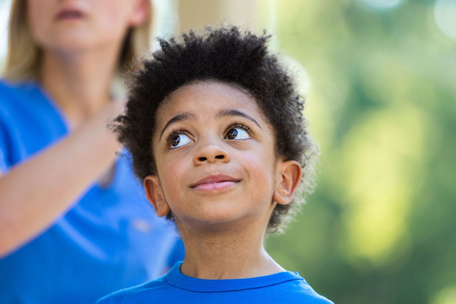 Young student in blue t-shirt looking up with curiosity and wonder.