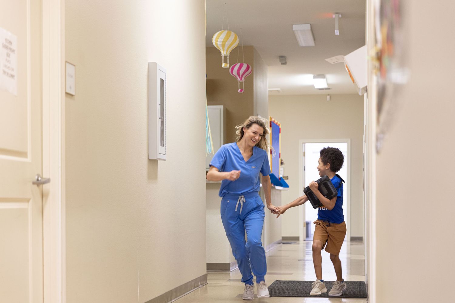 Medical professionals in blue scrubs running playfully down a bright hospital corridor.