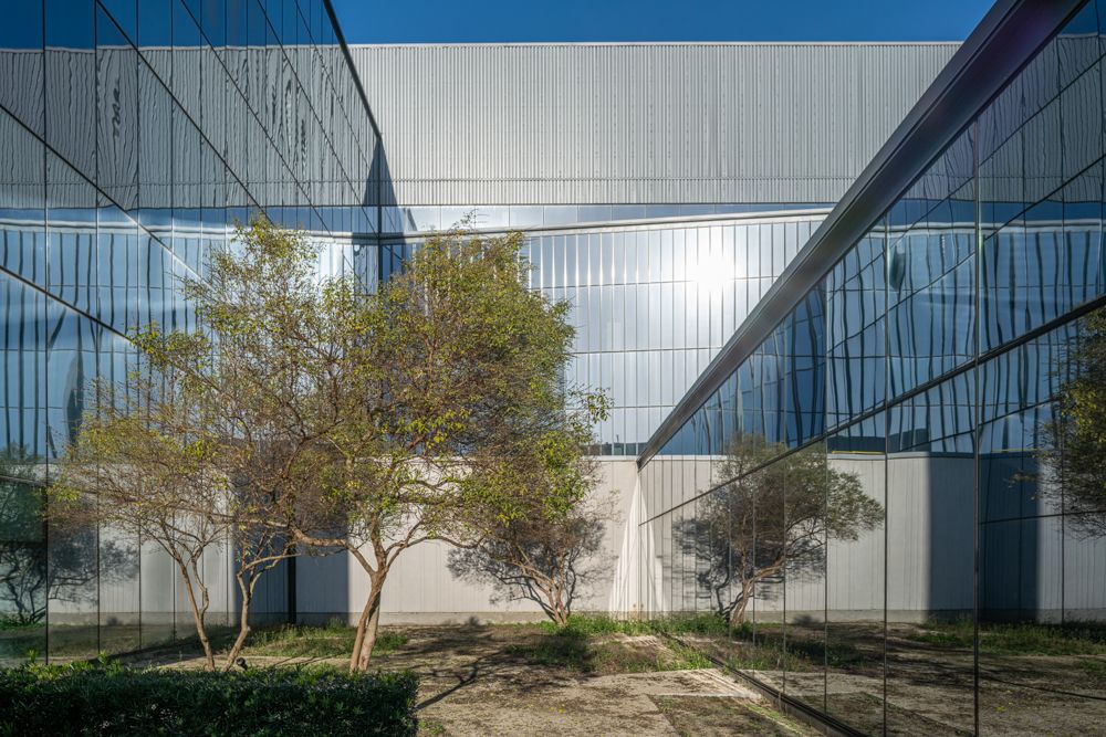 Modern glass building exterior with trees and reflecting surfaces in courtyard.