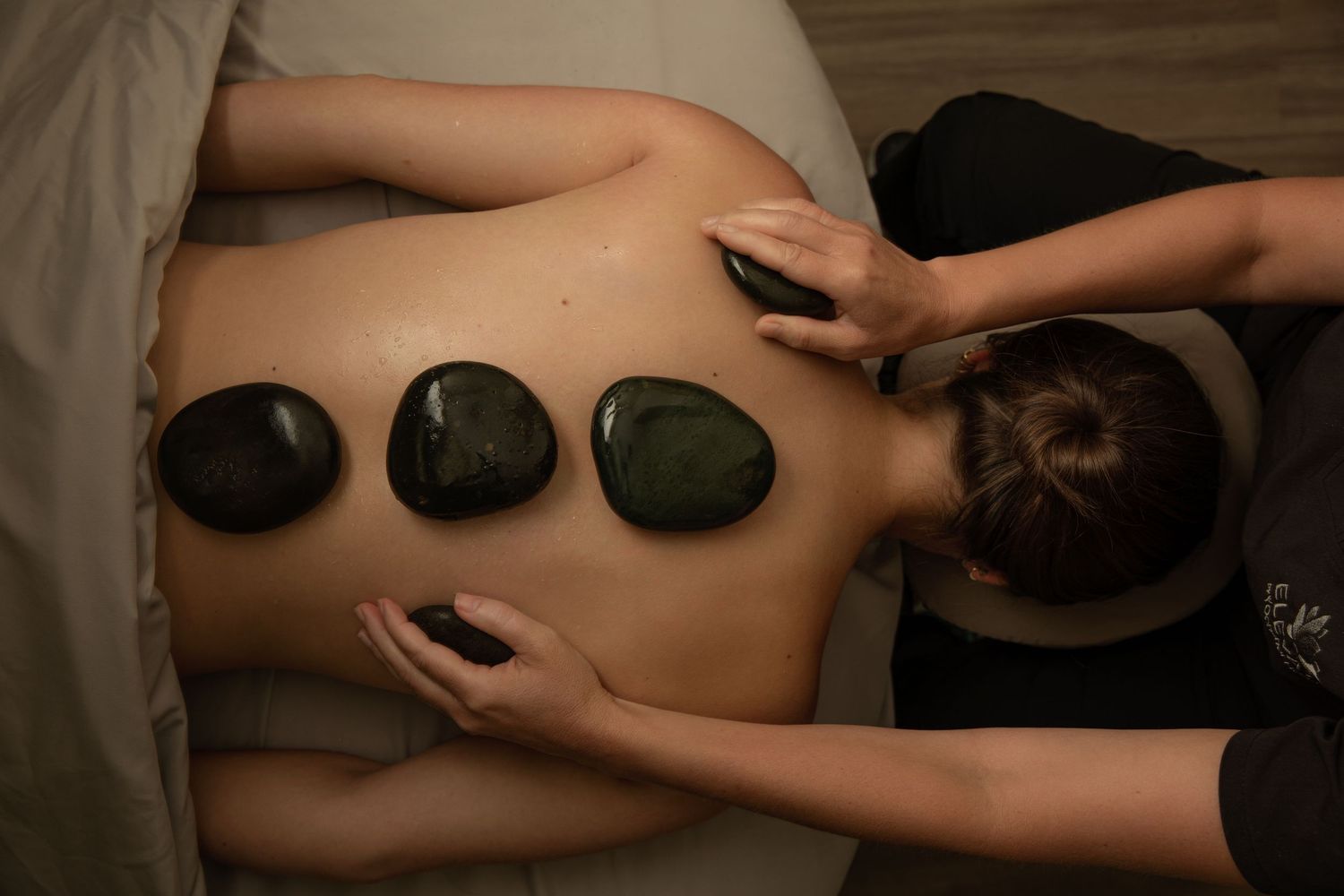 Hot stone massage therapy treatment with black stones placed along spine for relaxation and wellness.