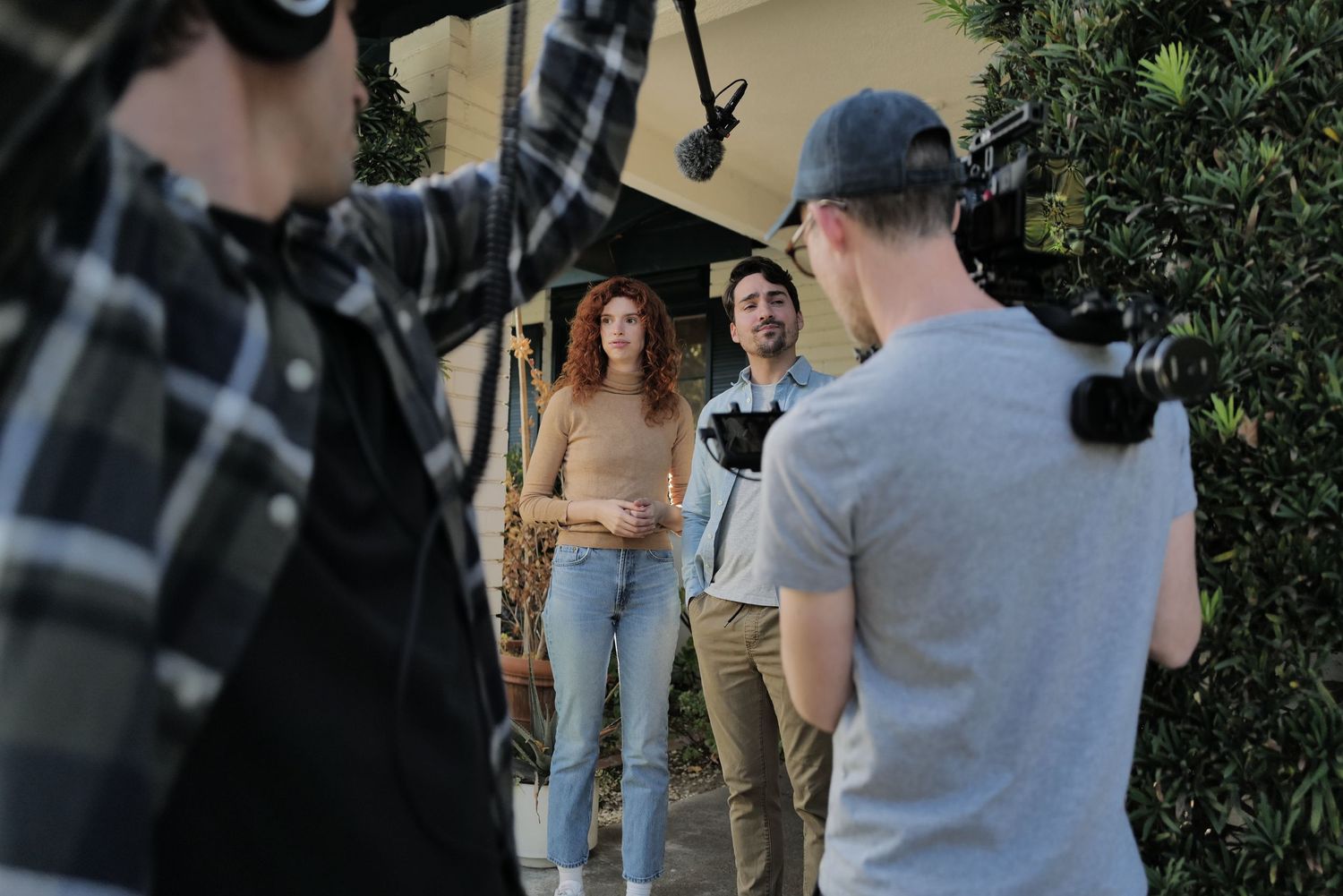 Film crew shooting outdoor scene with two actors, cameraman, and director on a sunny day.
