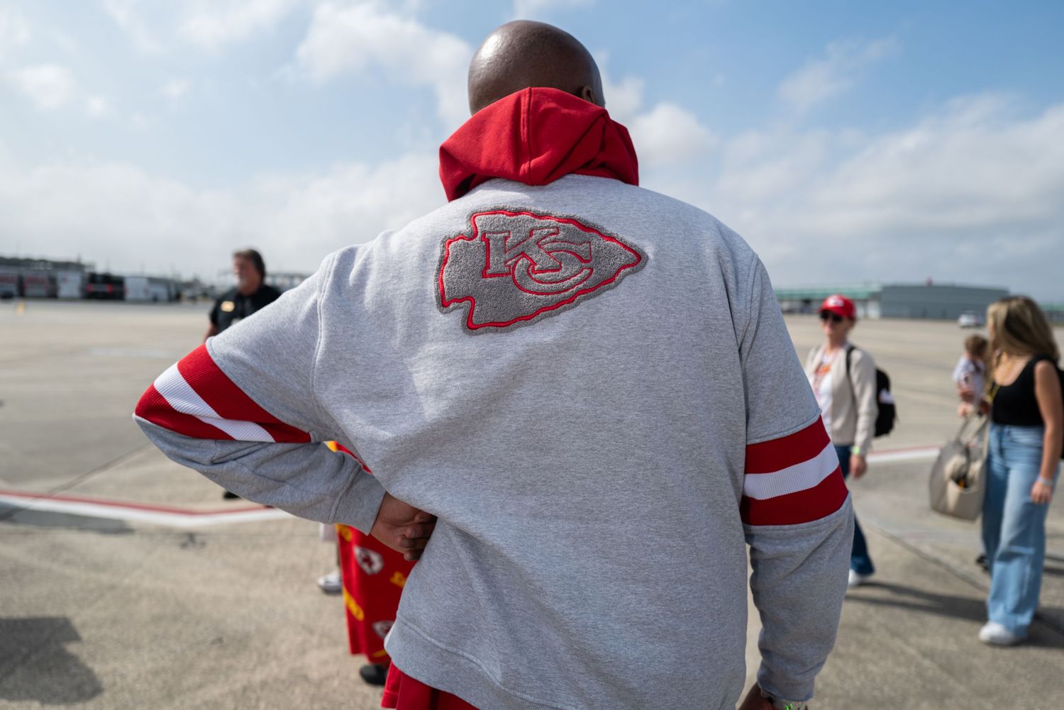 Person wearing Kansas City Chiefs jersey seen from behind on airport tarmac.