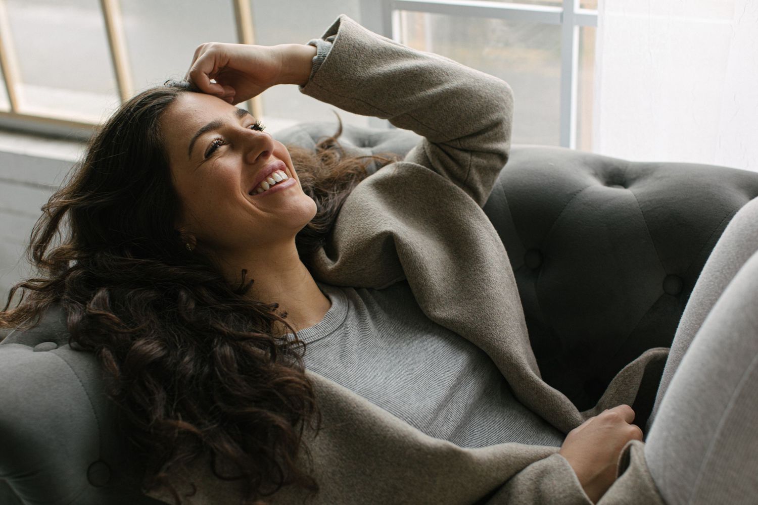 Relaxed candid moment on a grey couch by a window.