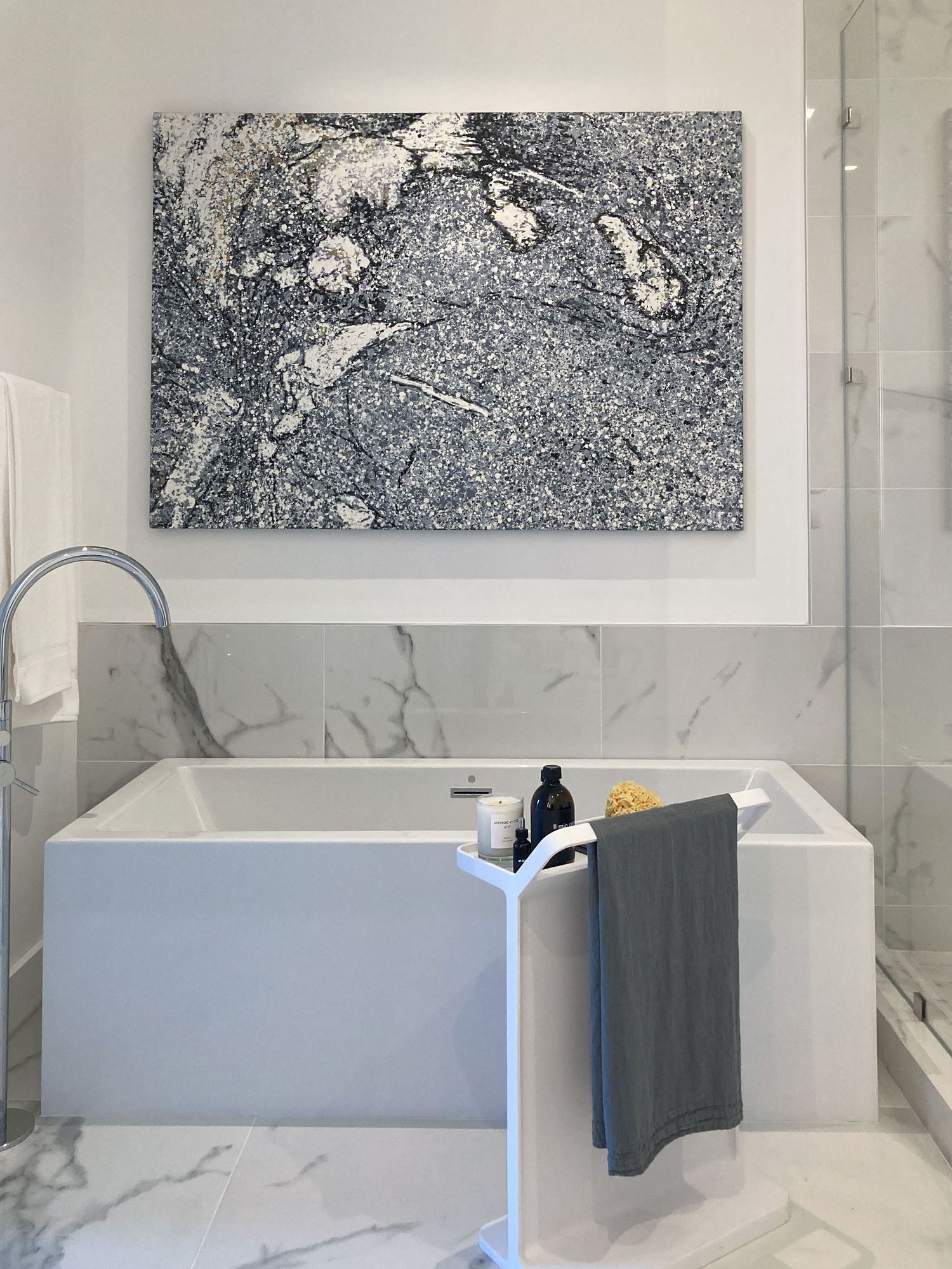 Modern bathroom interior with white marble walls and abstract black and white artwork above a freestanding bathtub.