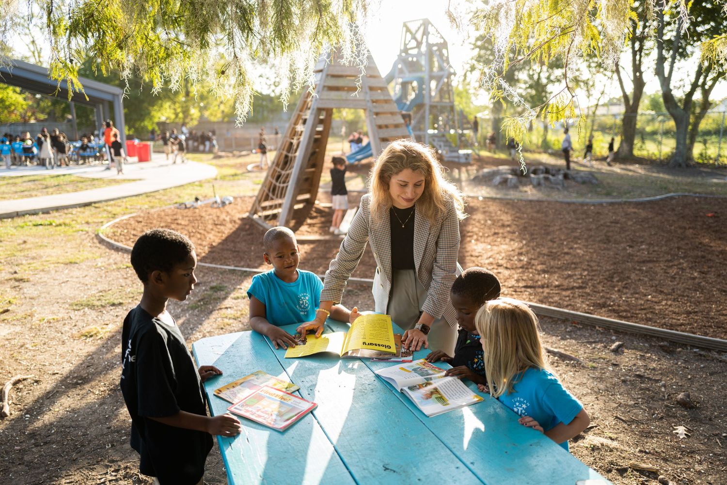 Teacher leading outdoor learning activity with children at picnic table.