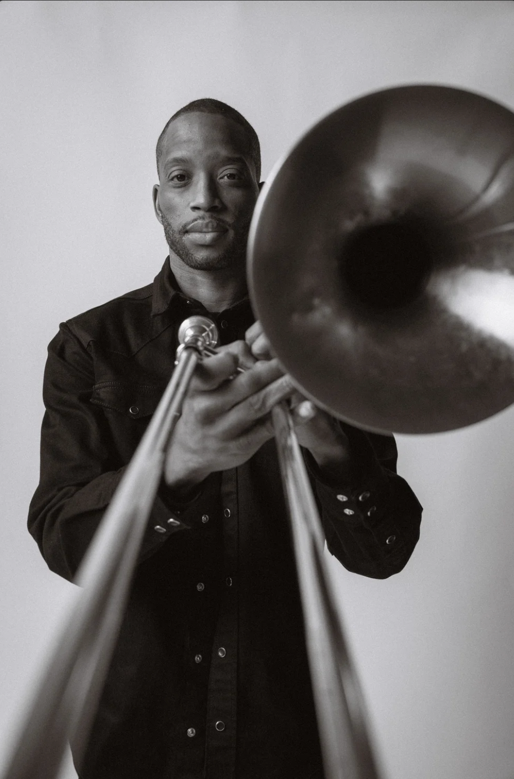 Black and white portrait of a musician holding a trombone while wearing a dark button-up shirt.