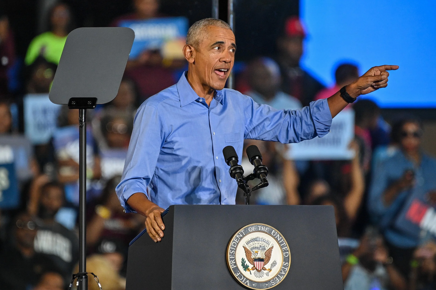 A speaker gestures while delivering remarks at a podium with the Vice Presidential seal during a public event.