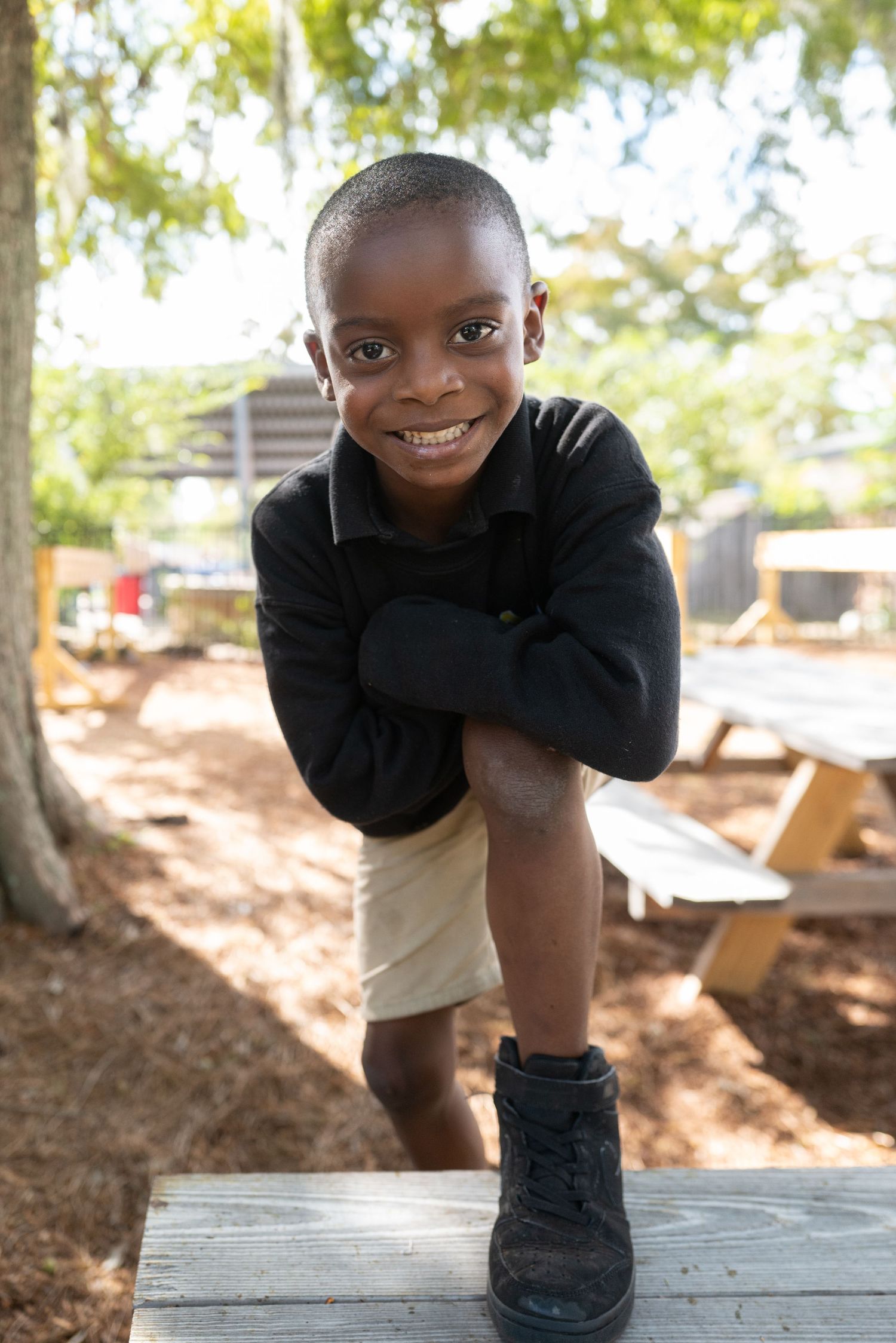 Child in black sweater posing playfully outdoors at playground.