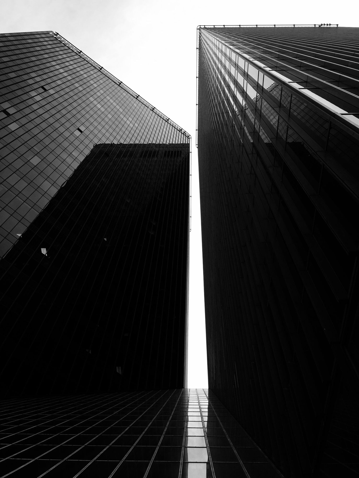 Low angle black and white shot of two modern skyscrapers converging against the sky.