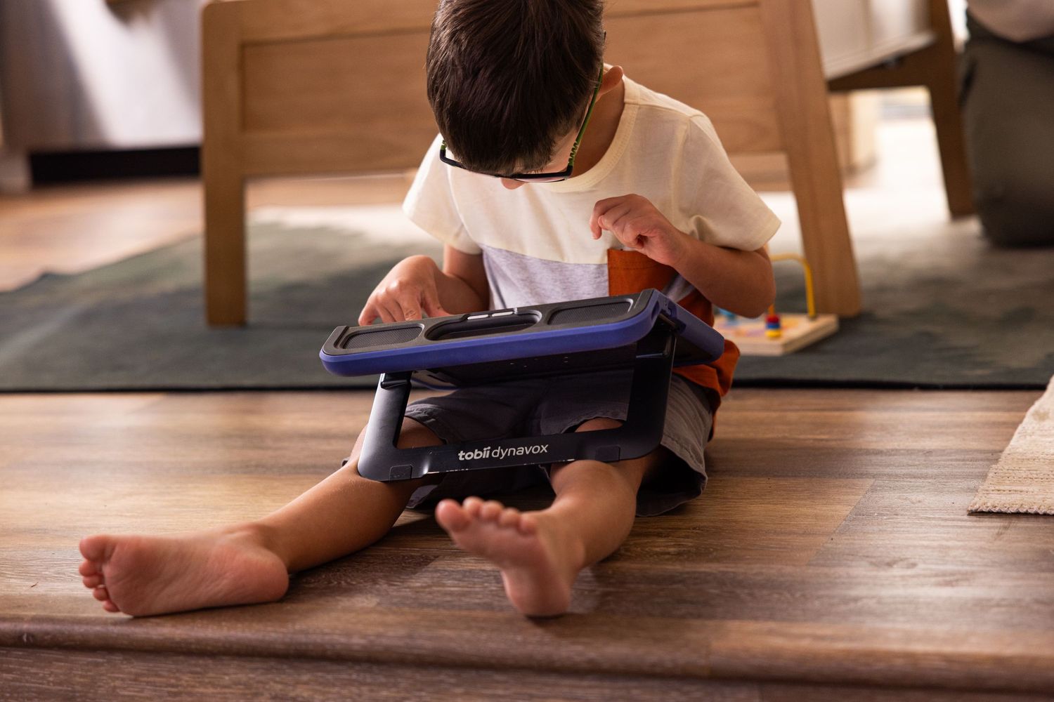 Child sitting on wooden floor using a tablet device with protective case.