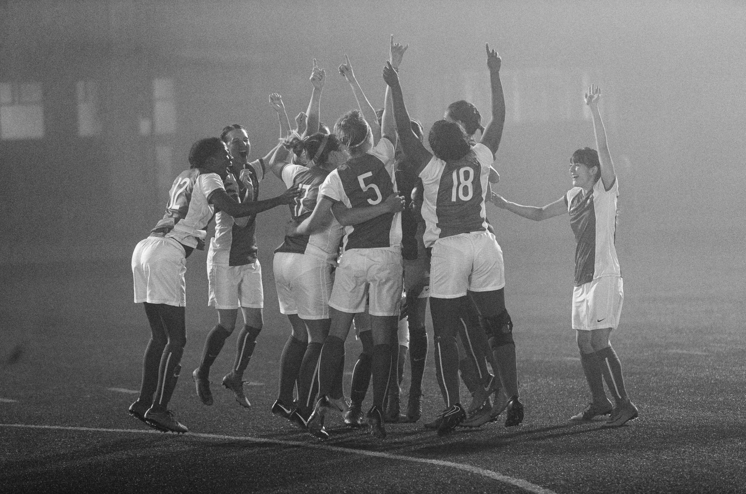 Team of soccer players celebrating victory together on misty field at night.