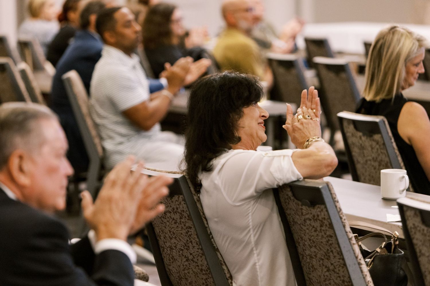 Conference attendees applaud during a presentation in a formal meeting room.