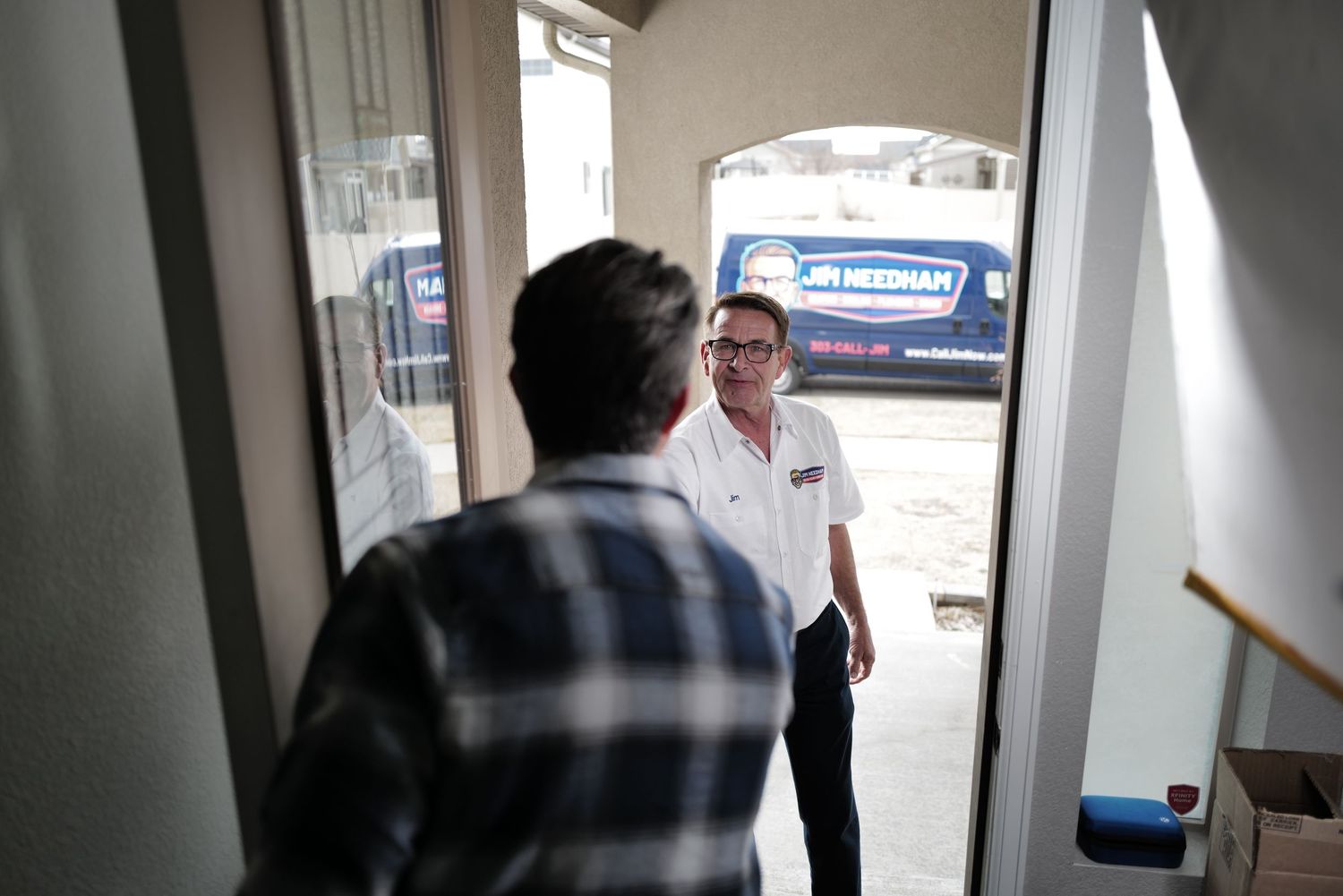 A service technician greets a customer at the front door of a home with a branded van visible outside.
